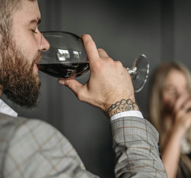 Sophisticated man in a gray suit savoring red wine at a stylish social gathering.