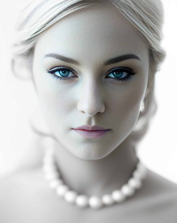 Elegant portrait of a young woman with porcelain skin, blue eyes, and a classic pearl necklace.