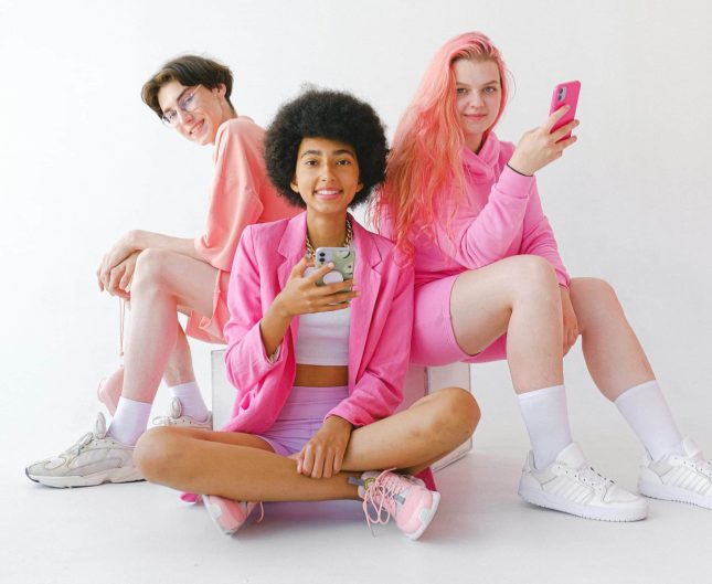 Three young women in pink outfits share a joyful moment in a bright, minimalist setting.