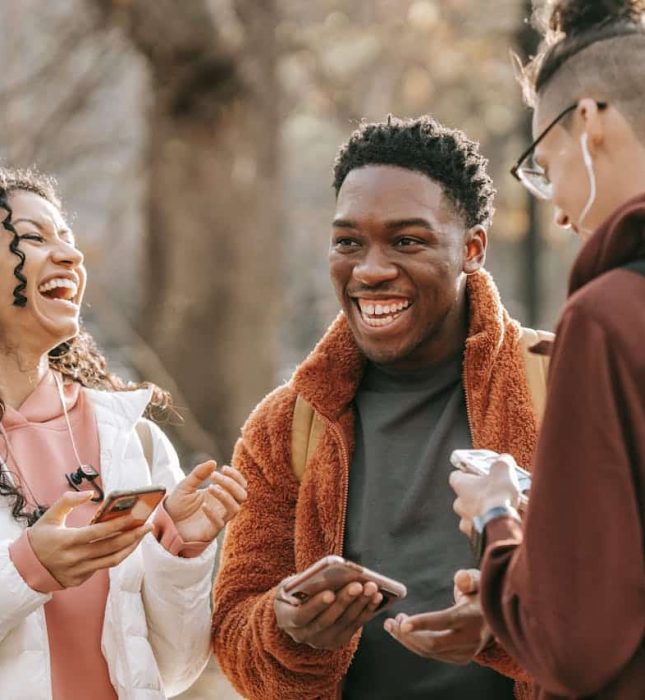 Friends laughing outdoors on an autumn day, enjoying each others company amidst colorful leaves.