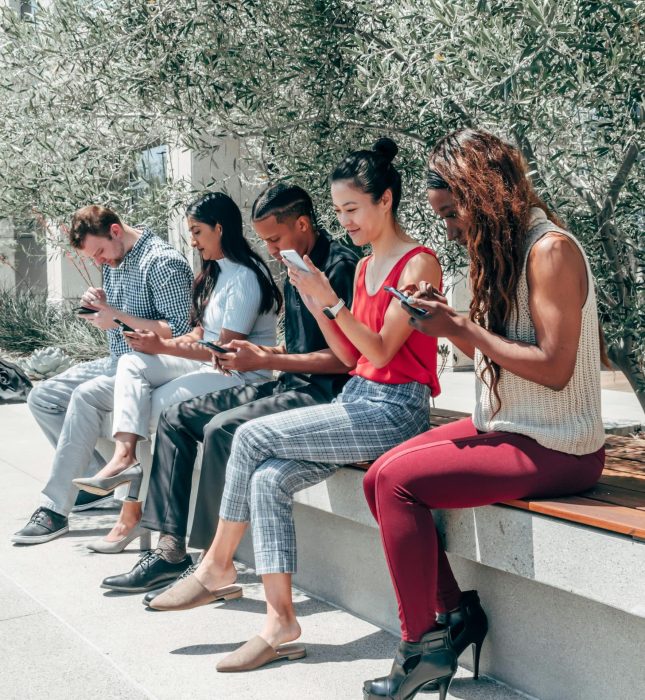 Friends connecting outdoors, engaged with mobile devices in a serene, green setting.