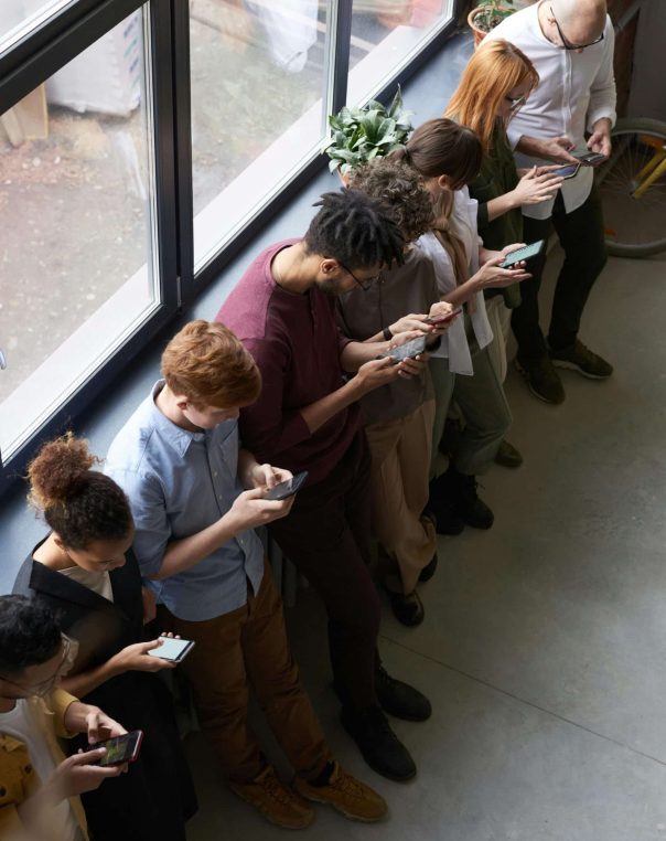 Diverse group of eight engaged with mobile devices in a bright, modern office setting.