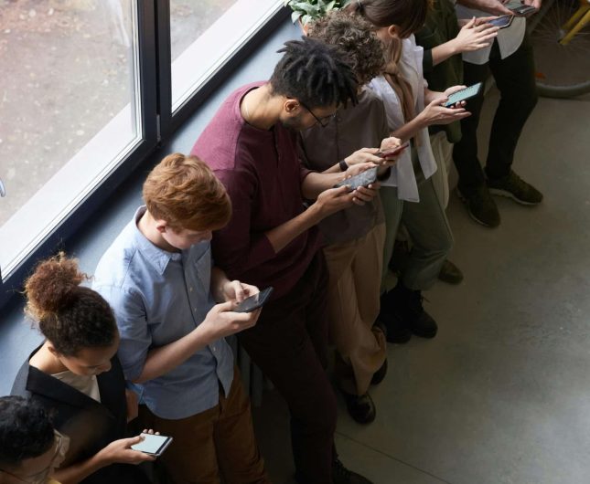 Diverse group of eight engaged with mobile devices in a bright, modern office setting.
