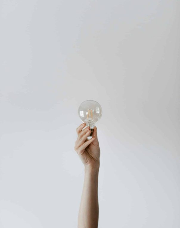 Hand reaching for a light bulb, symbolizing creativity and inspiration against a soft gray background.