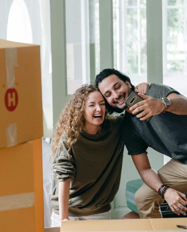 Happy couple joyfully celebrating their new home amid cardboard boxes and bright natural light.