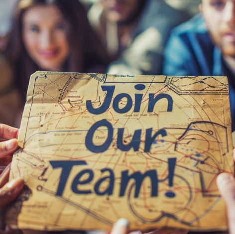 Diverse team inviting collaboration with a rustic Join Our Team! sign in a warm setting.