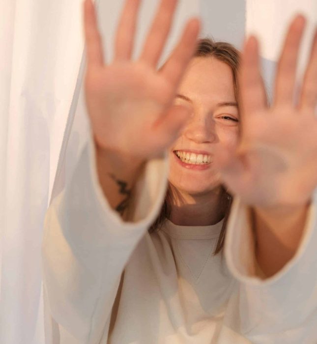 Joyful woman radiating happiness, playfully inviting connection against a soft backdrop.