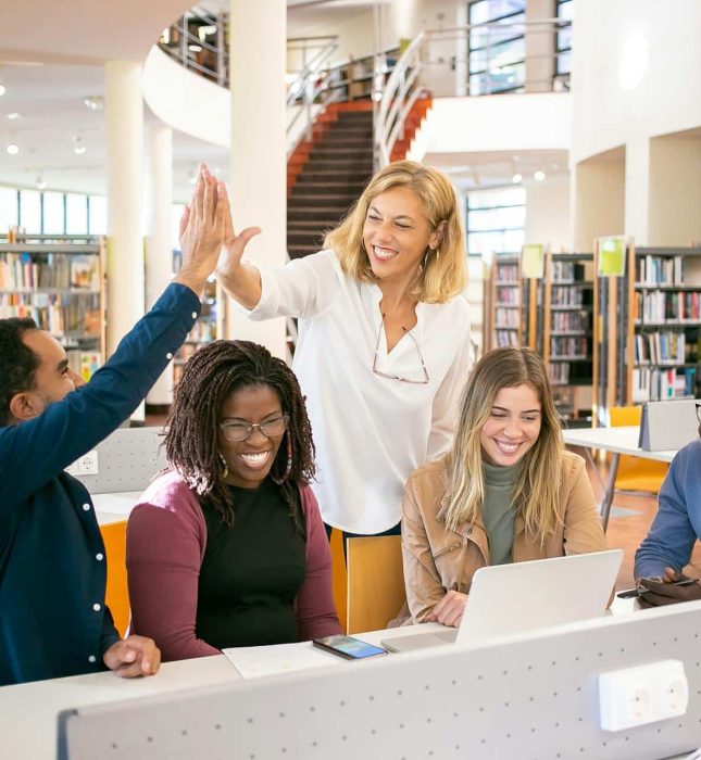 Diverse young professionals celebrate teamwork and collaboration in a bright, modern library.