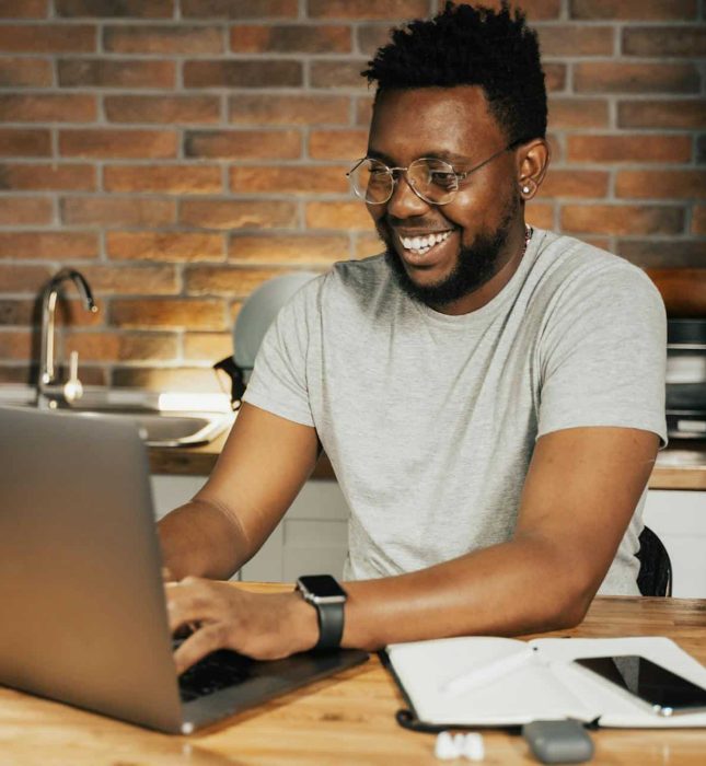 Man joyfully working on a laptop in a cozy, modern workspace with a brick wall.