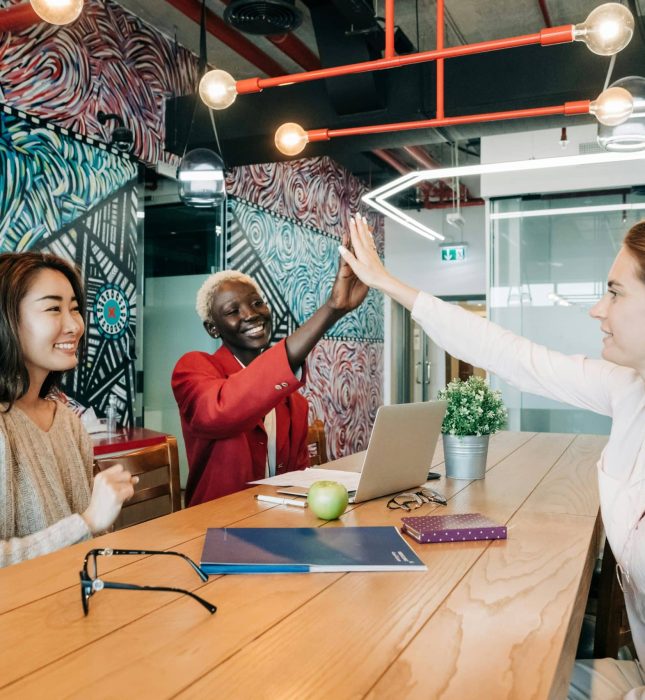 Diverse team celebrates success in a vibrant, creative workspace filled with color and collaboration.