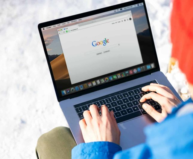 Person in red hat using laptop in snowy outdoor setting, blending technology with nature.