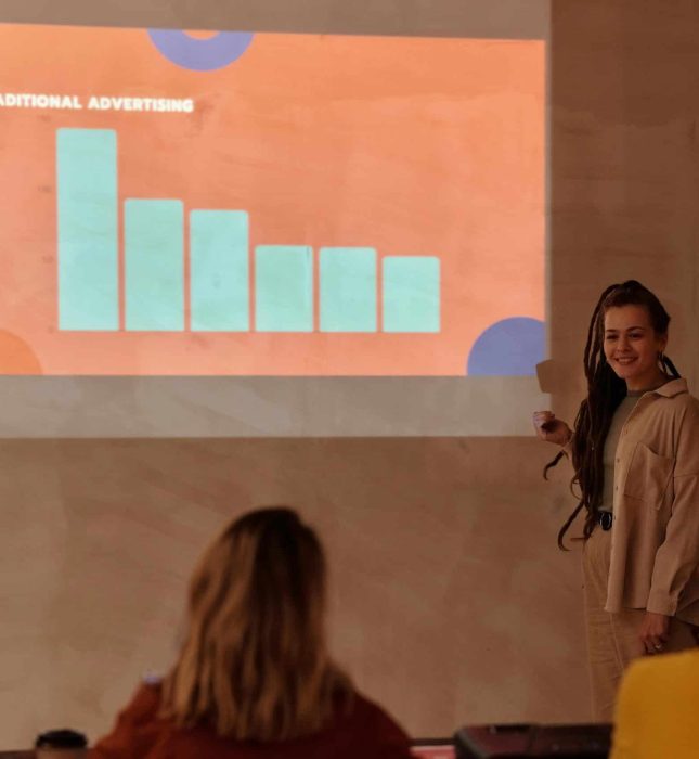 Young woman presents engaging data to attentive audience in a warm, modern learning space.