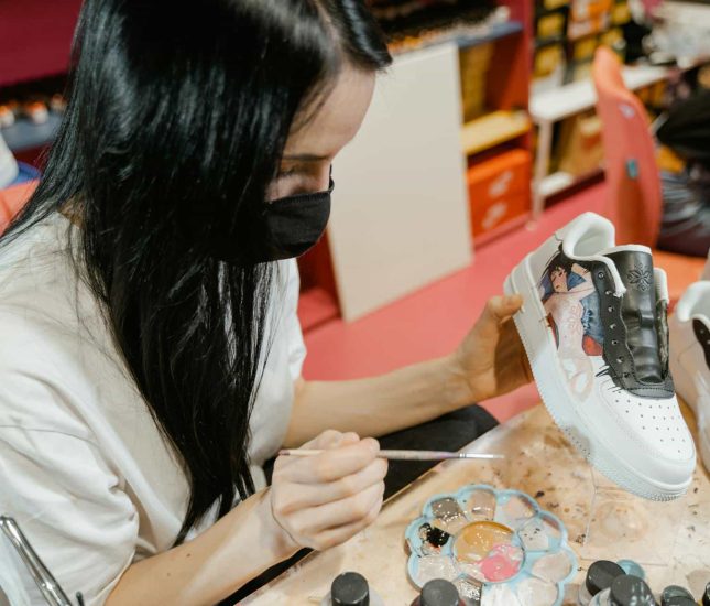 Young woman customizing sneakers with vibrant paints in her creative workspace.
