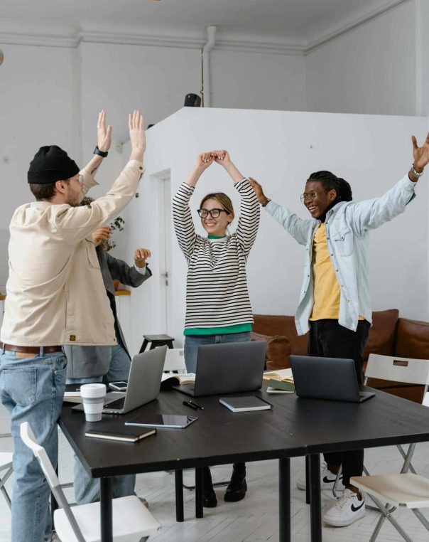 Team celebrates success in a bright, modern workspace with laptops and joyful expressions.