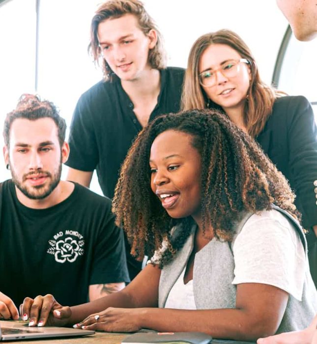 Team collaborating around a laptop in a bright, modern office setting.