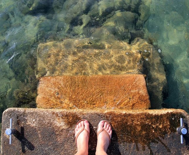 Worn stone steps invite you into crystal-clear waters, surrounded by natural beauty and sunlight.