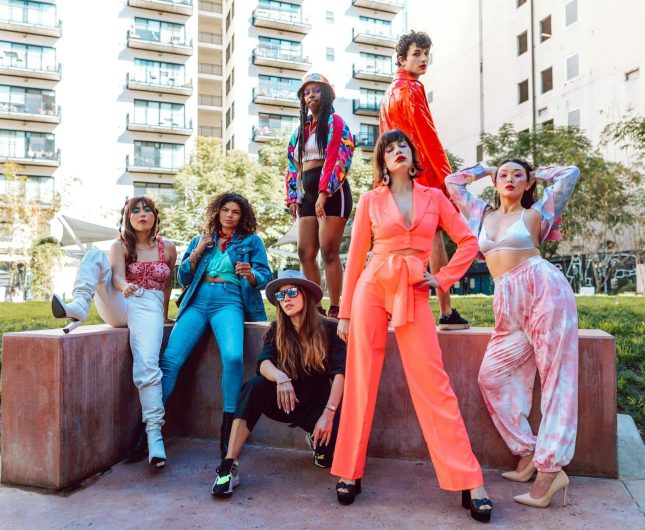 Seven empowered women in vibrant outfits pose confidently in an urban setting, celebrating individuality.