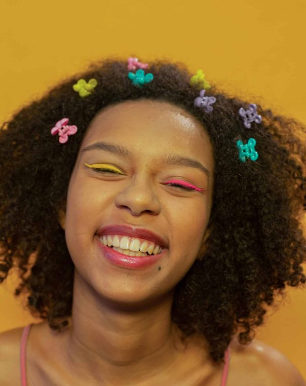 Joyful youth with colorful hair clips and vibrant makeup against a cheerful yellow background.