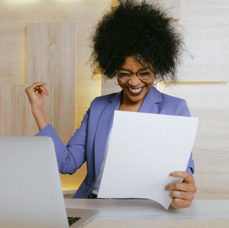 Joyful woman in lavender suit celebrates achievement in modern office setting.