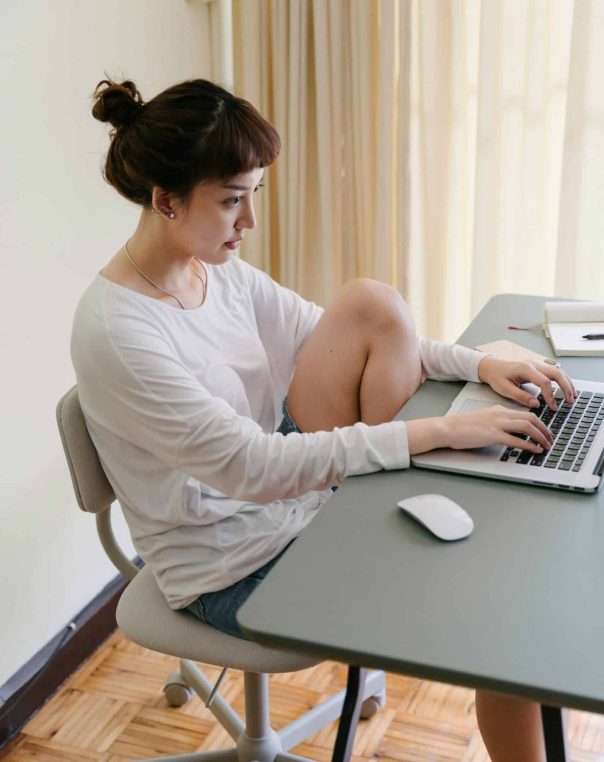 Relaxed woman working on a laptop at a minimalist desk in natural light.