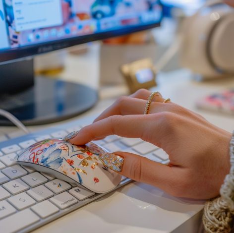 Elegant hand with glitter nails using a colorful floral mouse in a modern workspace.
