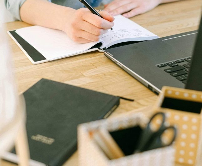 Focused individual writing in a serene, organized workspace with notebooks and a laptop.