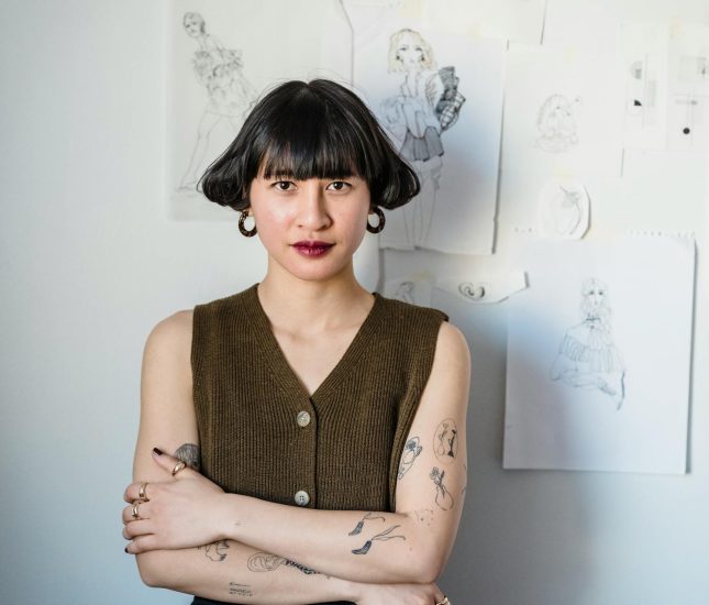Confident young artist with bob hairstyle in creative space surrounded by her sketches.
