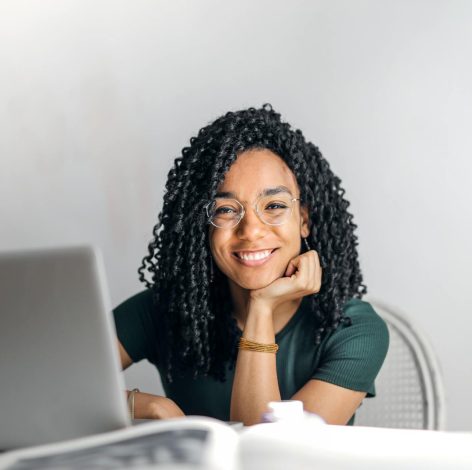 Joyful woman with curly hair working on laptop in a stylish, modern workspace.