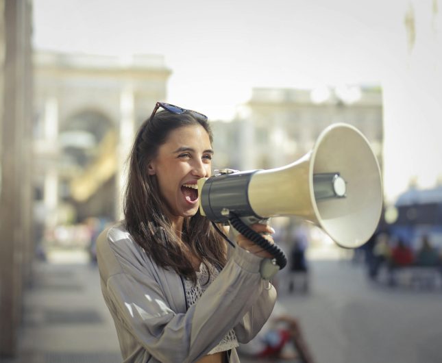 Confident young woman advocating passionately into a megaphone at a vibrant community rally.