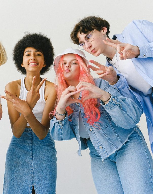 Four friends in trendy denim outfits share joy and friendship against a light backdrop.